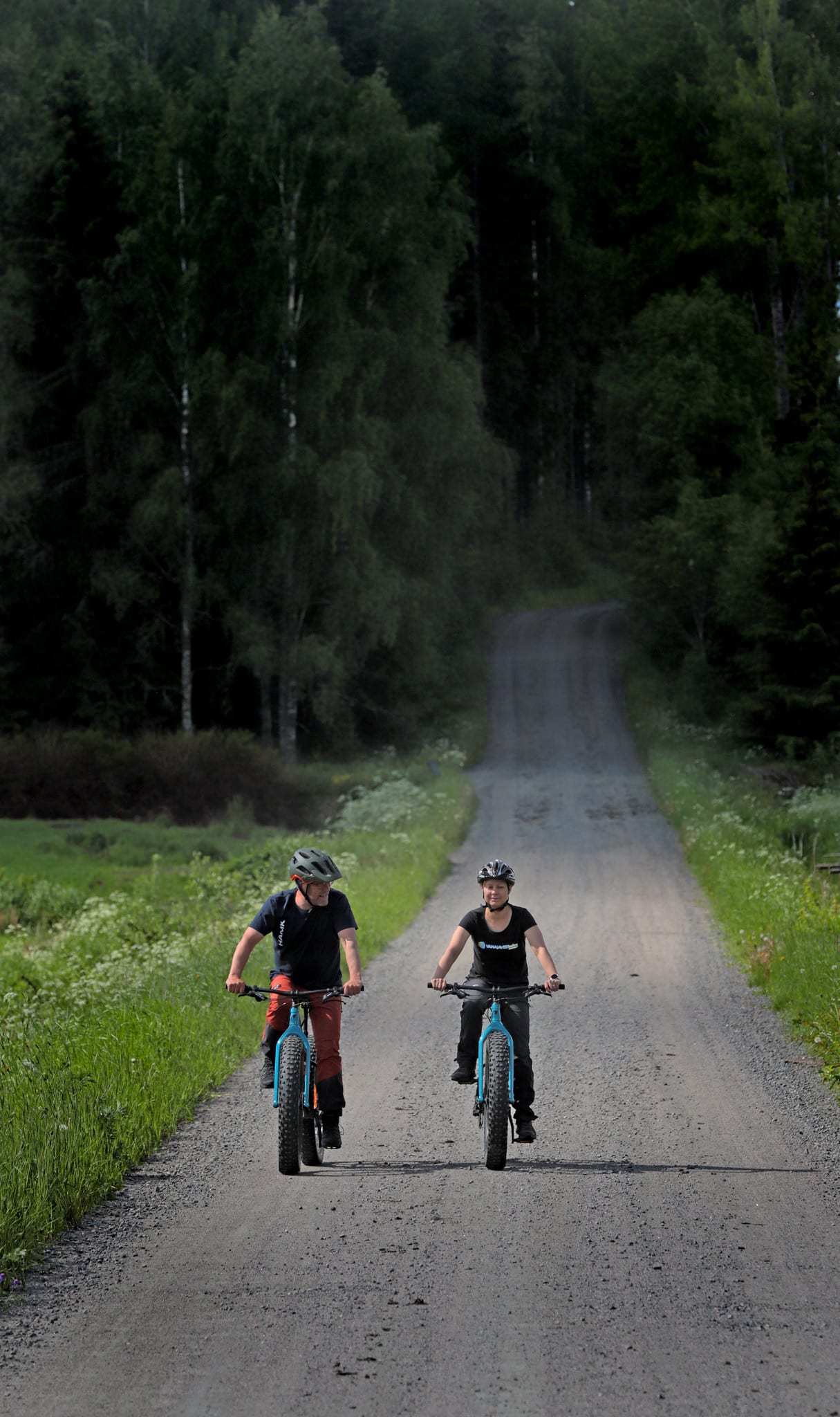 Kaksi pyöräilijää hiekkatiellä.