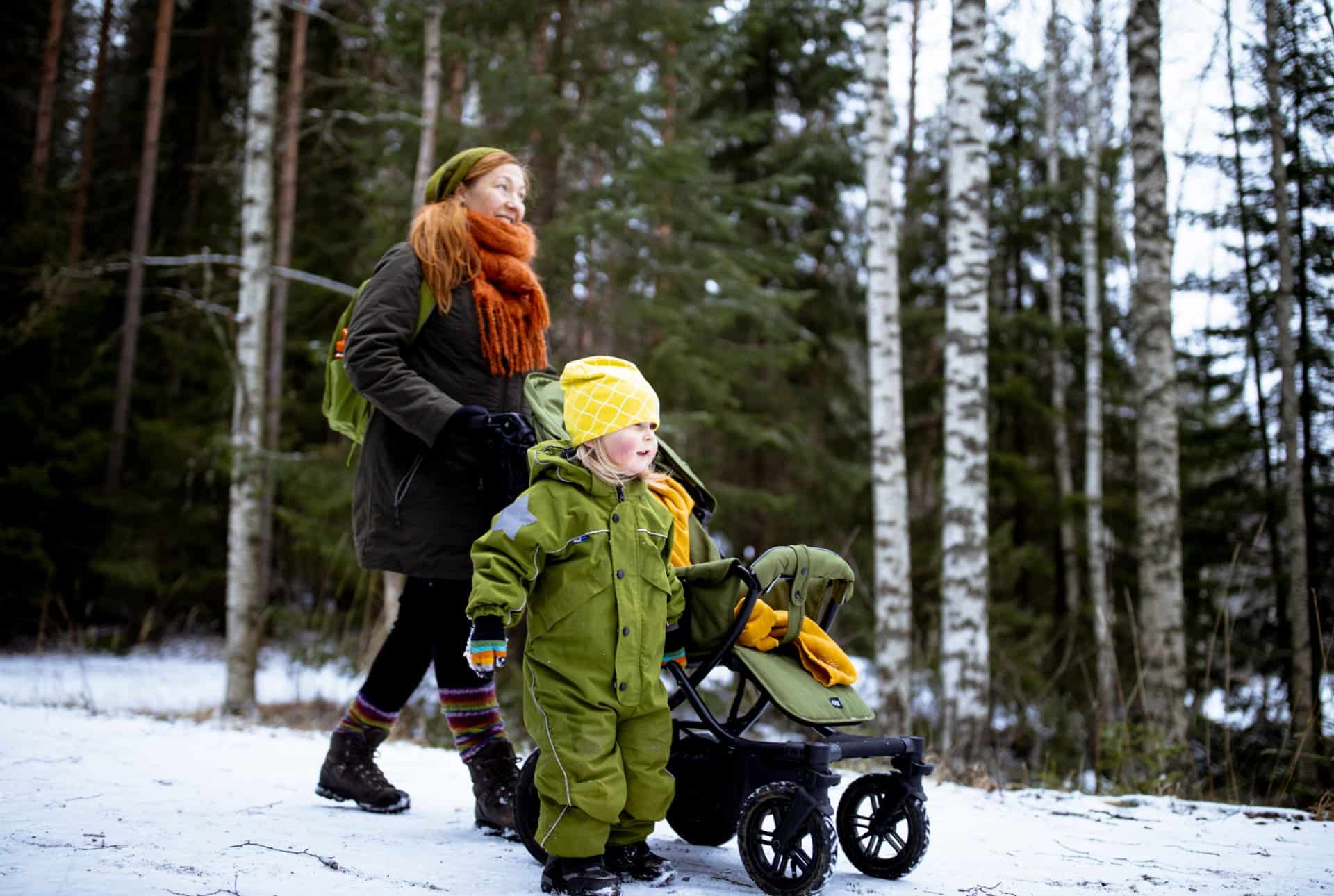 Neljä ihmistä kävelemässä suomaisemassa pitkospuilla, takana korkeita puita, joiden välistä pilkistää auringonsäteitä.