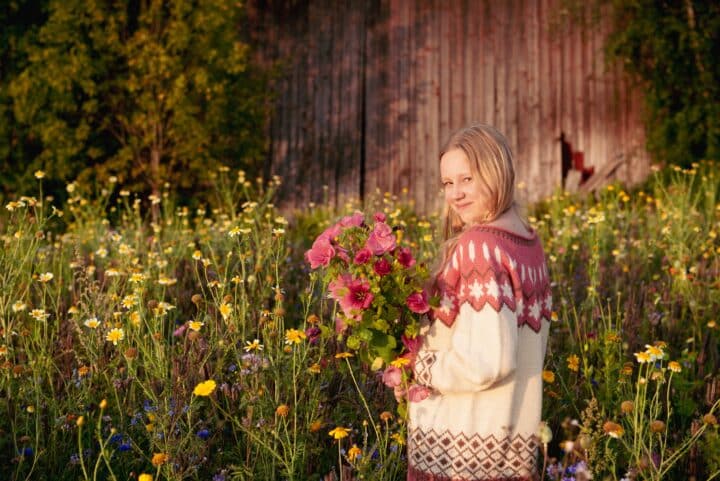 A girl is in the middle of a flower field. She is holding flower in her hands and smiling.