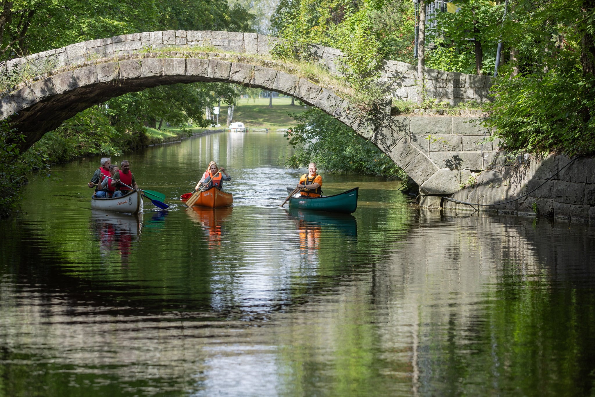 People in tree canoes paddling under the stone bridge.