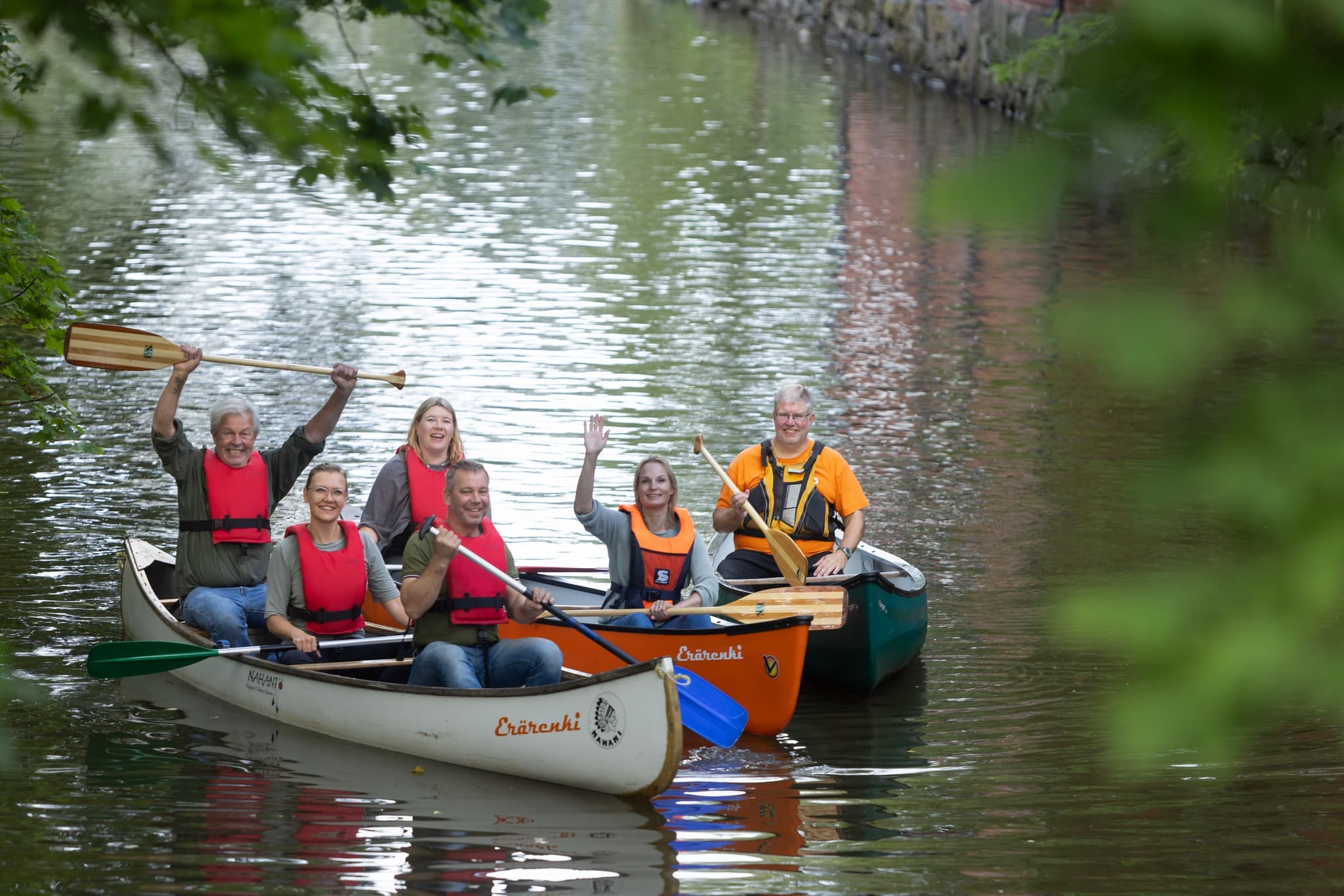 Group of people sitting in three canoes smiling and waving at the camera.