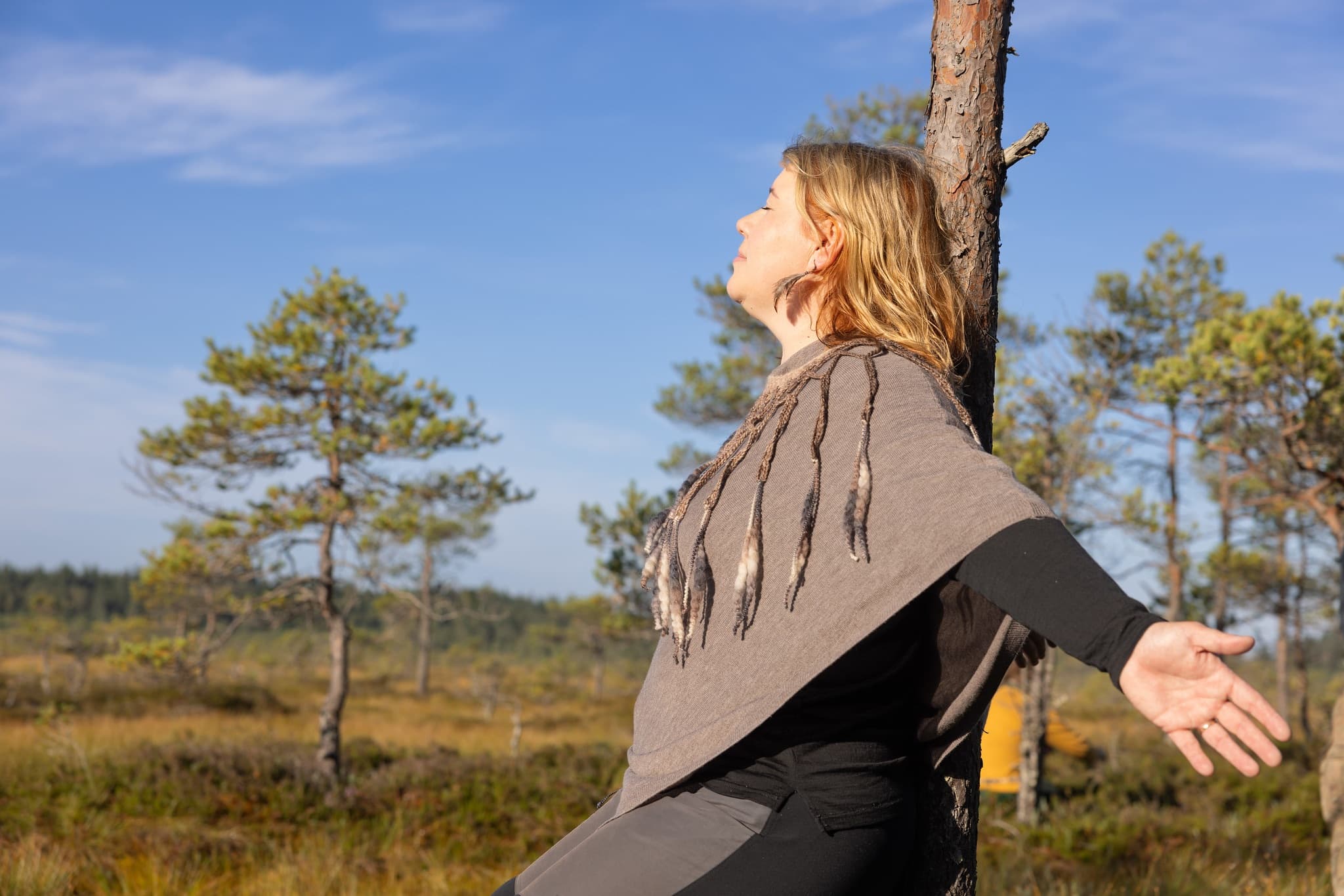 Woman leaning on a tree with her eyes closed in Torronsuo National Park, swamp scenery on the background.