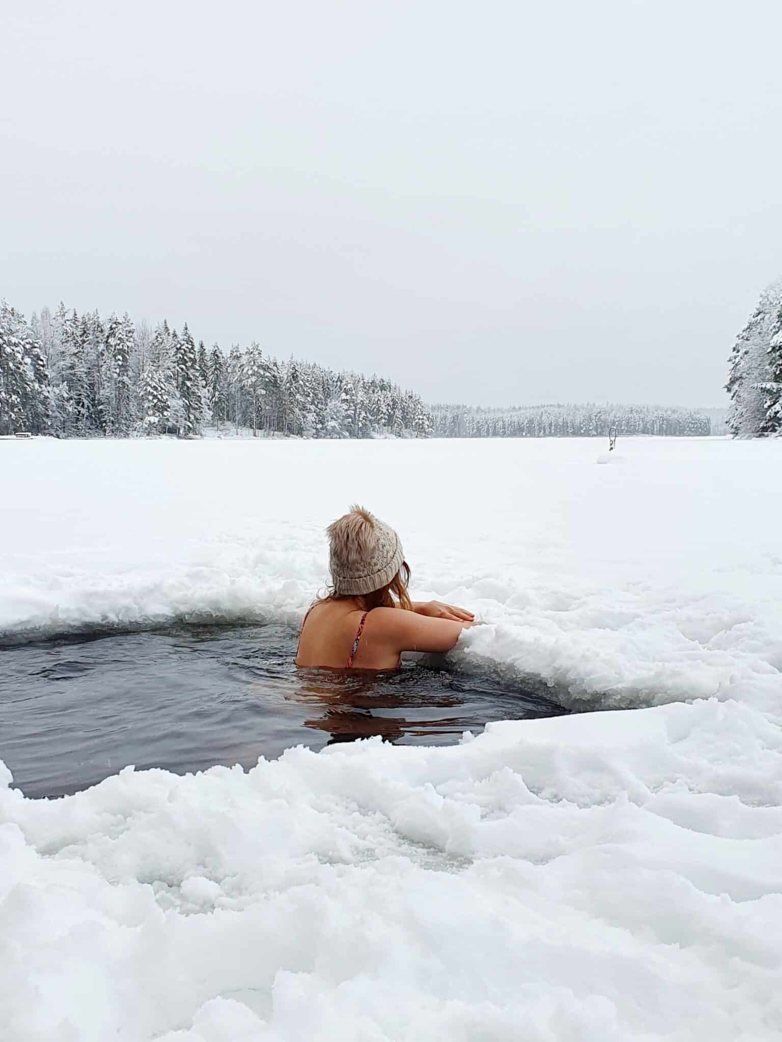 A woman is on a edge of ice looking over the snow covered lake.