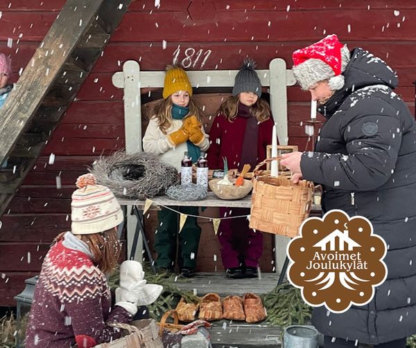 Lasten myyntipiste vanhan rakennuksen seinustalla ja aikuinen tonttulakki päässä ostoksilla lumihiutaleiden keskellä.