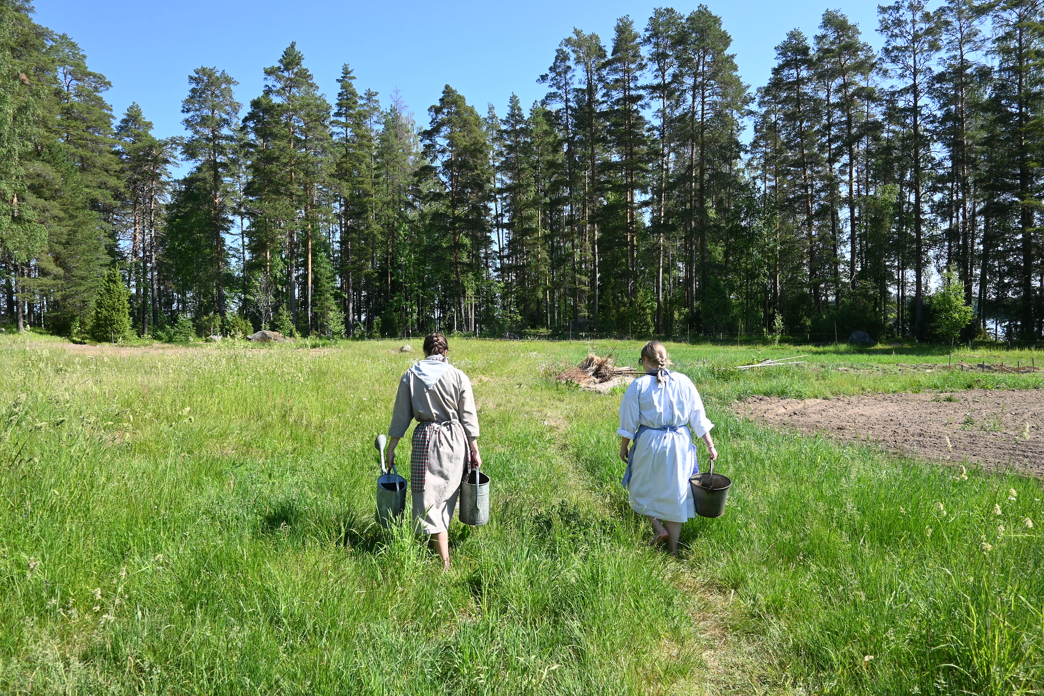 Persons are walking in a green field in Korteniemi. They are wearing old clothes.