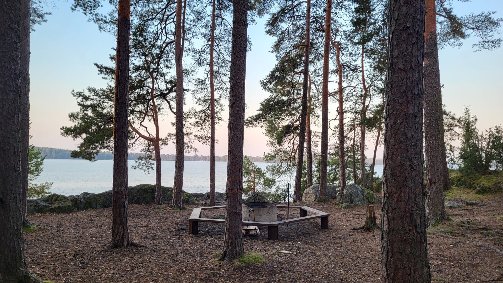 Kaksi ihmistä istuvat järven rannalla. Taustalla näkyy metsää.