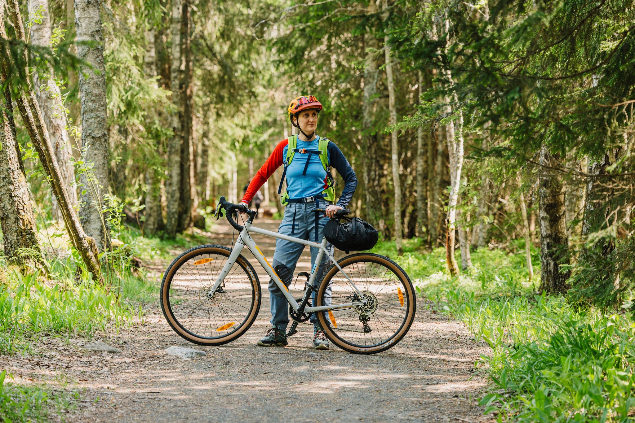 Nainen seisoo pyörän takana, hän on metsässä.