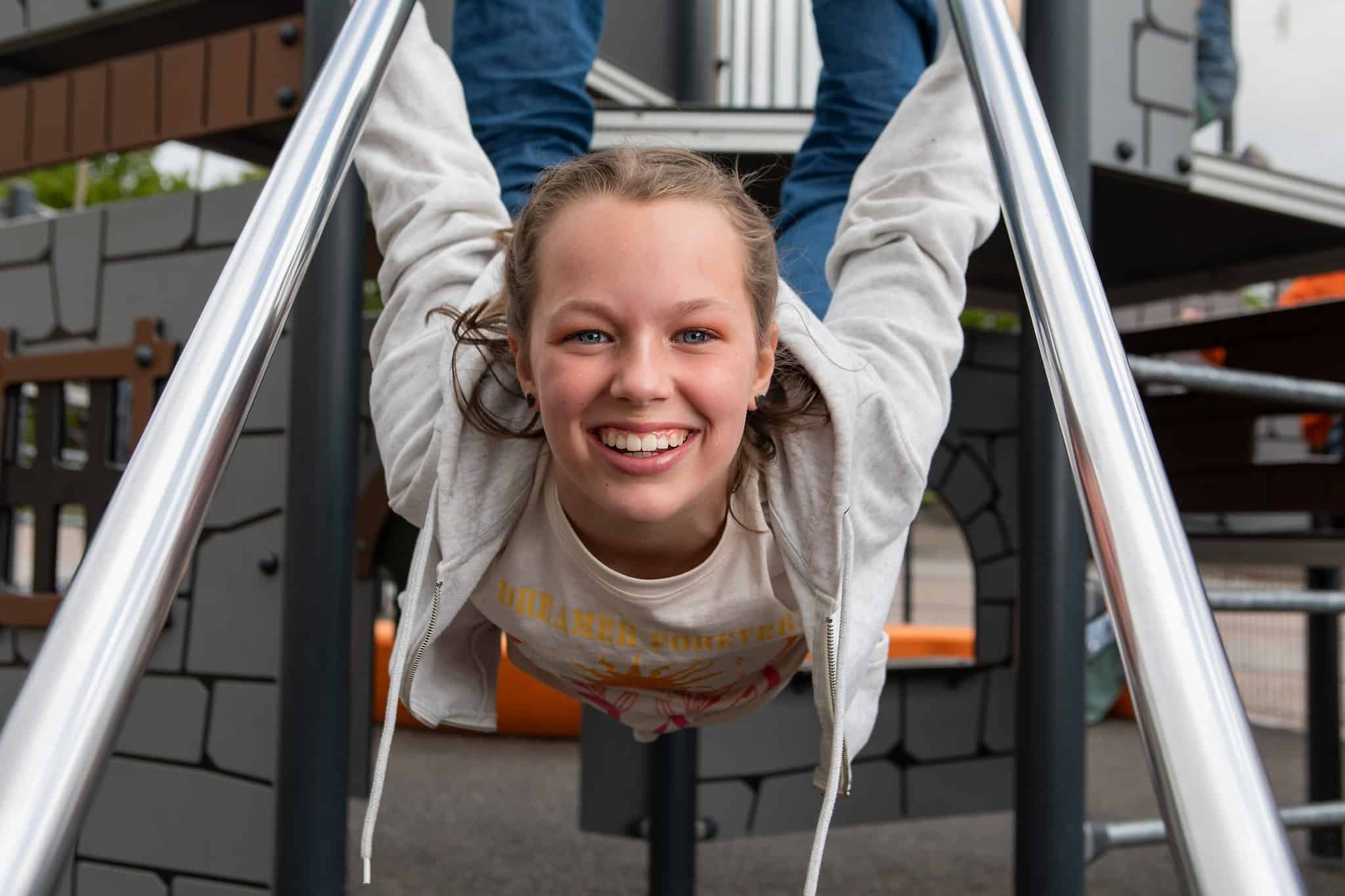 Teinityttö hymyilee ja roikkuu kiipeilytelineessä.