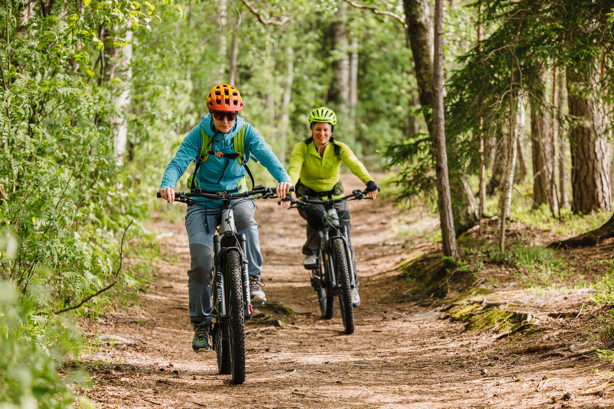 Two persons are cycling in a forest path.