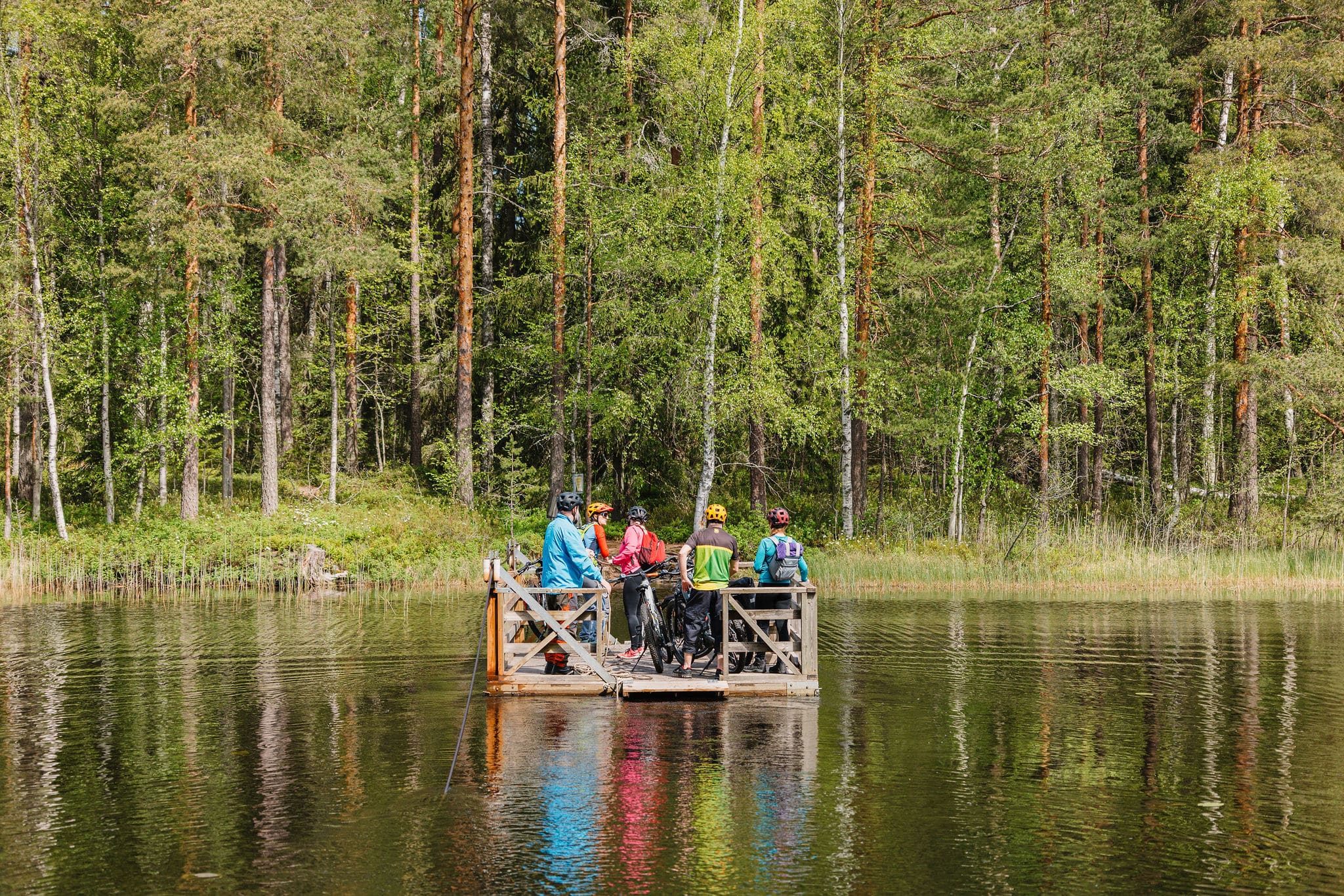 Ihmisiä on puisen lossin kyydissä ylittämässä vesistöä.